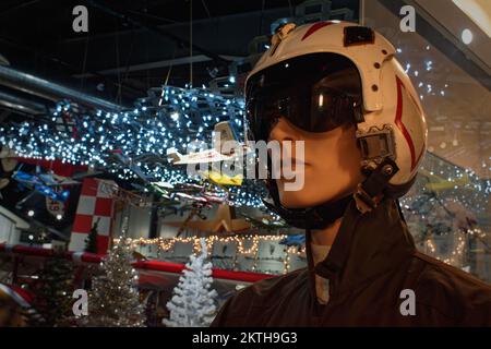 Un manichino vestito con una moderna divisa da jet piloti e casco si trova di fronte al pavimento del museo decorato a Natale presso il Museo dell'aviazione di New Hamp Foto Stock