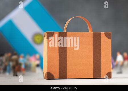 Valigia di cartone, personaggi di giocattoli di plastica e una bandiera su uno sfondo astratto, un concetto sul tema del trasferimento o dell'immigrazione in Argentina Foto Stock