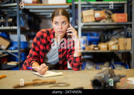 La lavoratrice prende un ordine su un telefono cellulare e prende appunti nel notebook Foto Stock