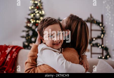 La madre tiene tra le braccia, abbraccio tenero, abbraccia dolcemente bambino bambino figlio ragazzo in background di Natale Foto Stock