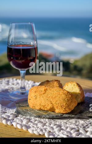 Abbinamento di cibo e bevande portoghesi, bicchiere di vino porto bruno e coccodrillo pastais de bacalhau, servito all'aperto con vista sul blu soleggiato Atla Foto Stock