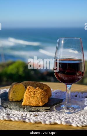 Abbinamento di cibo e bevande portoghesi, bicchiere di vino porto bruno e coccodrillo pastais de bacalhau, servito all'aperto con vista sul blu soleggiato Atla Foto Stock