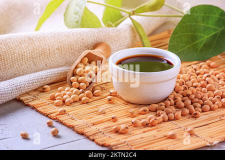 Salsa di soia con fagioli di soia sparsi su un tovagliolo di bambù sullo sfondo del burlap e ramificazione giovani baccelli verdi di soia, closeup con fo selettivo Foto Stock