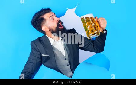 Soddisfa l'uomo bearded in vestito con tazza di birra guardando attraverso il foro di carta. Oktoberfest. Foto Stock