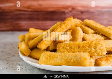 Il pesce si attacca in un croccante dorato che breading primo piano sul piatto bianco sul tavolo da cucina, fuoco selettivo Foto Stock