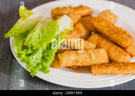 Bastoncini croccanti di pesce fritti serviti con lattuga verde primo piano su piatto bianco sul tavolo Foto Stock