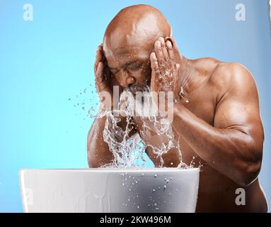 Cura della pelle, spruzzi d'acqua e uomo nero per la cura della pelle senior mentre il viso lavaggio per una pelle luminosa, sana e pulita su sfondo blu. Modello africano in Foto Stock