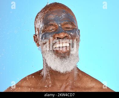 Viso, spruzzi d'acqua e uomo nero anziano in maschera di argilla in studio isolato su uno sfondo blu. Pulizia, pensionati e anziani maschi dalla Nigeria lavaggio Foto Stock