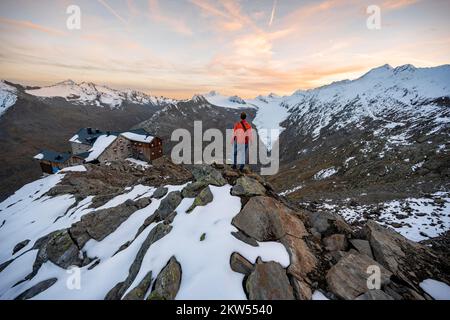 Escursionista guardando il panorama di montagna e il ghiacciaio, rifugio Ramolhaus in autunno con la neve, al tramonto, vista del Gurgler ferner con la cima Hochwilde An Foto Stock