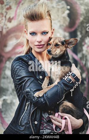 L'unico animale domestico per una rockstar come me. Ritratto corto di una giovane donna edgy che tiene il suo piccolo cane in un ambiente urbano. Foto Stock