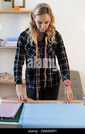 Ritratto di designer al lavoro con tessuto. Adattare la misura della quantità di materiale necessaria per il tessuto da cucire. Sforzo di marinaio sul lavoro. Comò che fa vestire Foto Stock