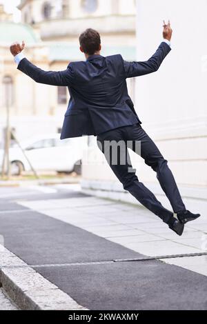 In cima al mondo degli affari. Ripresa da dietro di un uomo d'affari che salta per la gioia su un marciapiede della città. Foto Stock