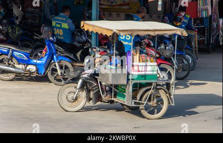 SAMUT PRAKAN, THAILANDIA, ottobre 19 2022, un distributore di gelati guida una moto a tre ruote lungo una strada cittadina Foto Stock