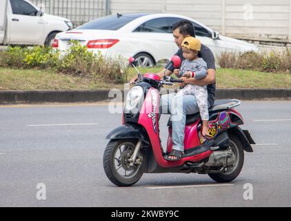 RATCHABURI, THAILANDIA, 16 2022 NOVEMBRE, Un padre porta un bambino piccolo tra le braccia su una moto in movimento Foto Stock