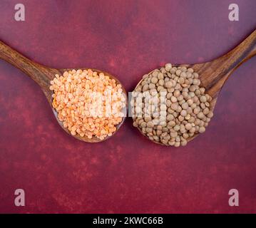 lenticchie rosse e verdi non raffreddate su cucchiai di legno di teak su uno sfondo rosso scuro bordeaux Foto Stock