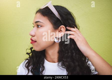 Bella, giovane, elegante e spensierata nero americano africano millennial donna. Capelli ricci lunghi, con occhiali da sole sulla testa, in piedi contro un lime Foto Stock