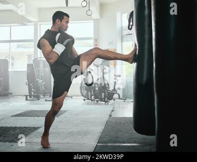 Atleta maschile calciare una borsa da punzonatura in una palestra mentre si pratica, allenamento e esercizio di fitness. Forte professionista combattente o atletico uomo in una salute Foto Stock