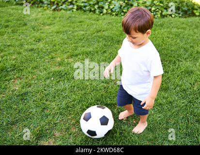 I veri giocatori imparano il gioco passo dopo passo. un adorabile ragazzino che gioca con una palla da calcio all'aperto. Foto Stock