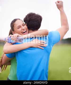Dargli un sostegno positivo. Una giovane donna che abbraccia il suo ragazzo su un campo sportivo mentre celebra una vittoria. Foto Stock