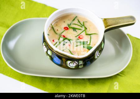 Minestra di verdure miste con porro e peperoncino in un recipiente rurale decorativo sul piatto, tovagliolo verde. Foto Stock