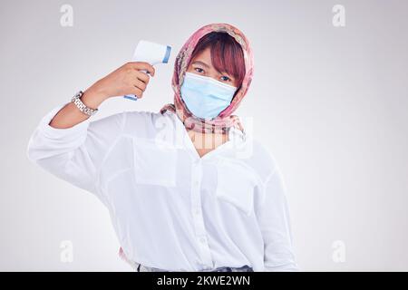 Donna musulmana, maschera facciale e termometro a pistola su sfondo bianco studio per marketing, virus e mockup sanitario. Ritratto del modello islam in Foto Stock