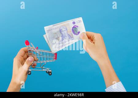 La mano della donna mette una libbra britannica nel carrello di shopping. Il concetto di risparmio nei negozi e nella spesa quotidiana Foto Stock