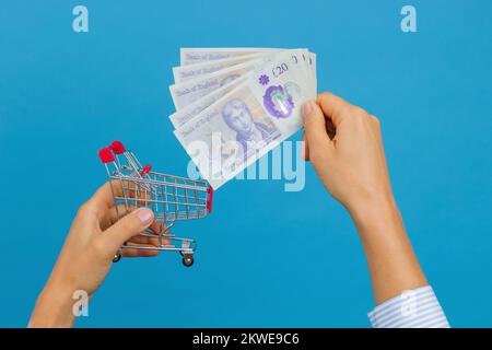 La mano della donna mette una libbra britannica nel carrello di shopping. Il concetto di risparmio nei negozi e nella spesa quotidiana Foto Stock