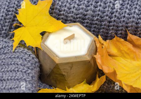 Candela in una pentola di cemento con uno stoppino di legno e foglie autunnali. Home comfort autunnale Foto Stock