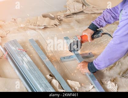 Una mano maschio senza guanti taglia pezzi di barra di acciaio con una smerigliatrice angolare. Taglio di acciaio inframmezzato da scintille in cantiere. Foto Stock