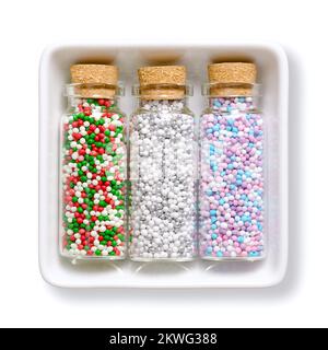 Nonpareils, in bottiglie di vetro, in ciotola bianca. Inverno e natale mix colorati di confetteria commestibile di piccole palle di zucchero. Centinaia e migliaia. Foto Stock