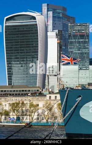 Bandiera di Union Jack a prua della HMS Belfast di fronte ai blocchi di uffici della City of London. Foto Stock