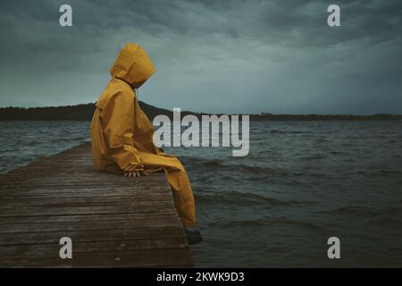 Misteriosa figura incappucciata seduta sul molo del lago Foto Stock