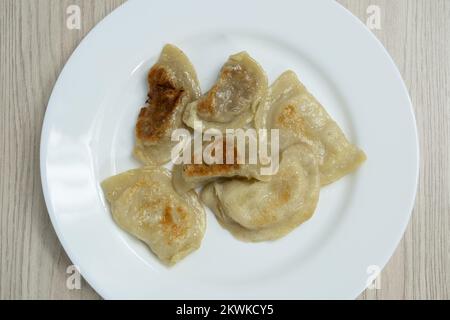 Gnocchi fritti con cavolo, formaggio e patate su un piatto bianco con lardo. La pelle è marrone e marrone. Foto Stock