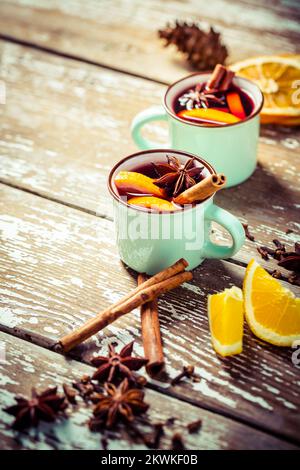 VIN brulé in tazze rustiche con spezie e agrumi su fondo in legno Foto Stock