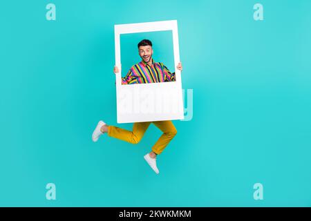 Foto a tutta lunghezza del corpo di salto funky aria trampolino uomo indossare retrò vecchi abiti di moda tenere carta cornice cadre evento isolato su sfondo blu Foto Stock