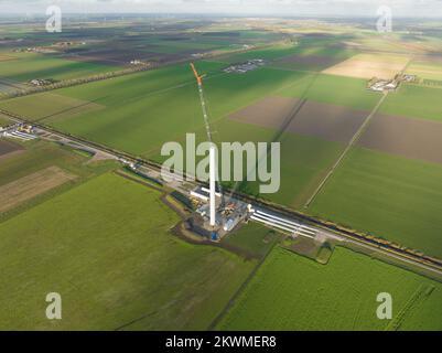 Processo di costruzione di turbine eoliche costruzione di mulini a vento con gru. Parti della turbina eolica, alloggiamento, mozzo, pale in loco. Drone aereo in alto Foto Stock