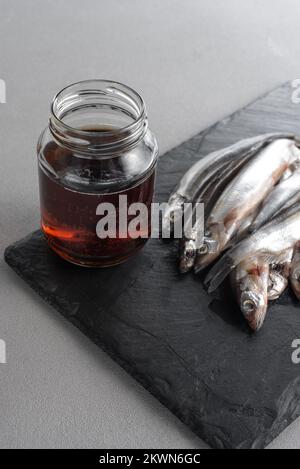 Il garum è una salsa di pesce fermentata. Preparato per fermentazione a base di pesce, salsa al garum salato in bottiglia su fondo grigio. Garum salsa di pesce fatta da Foto Stock