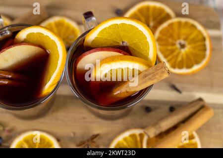VIN brulé in bicchieri di vetro, vino rosso caldo bevande alcoliche su tavolo di legno decorato con bastoncini di cannella e fette di arancia secca, vista dall'alto Foto Stock