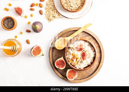 deliziosa colazione sana, farinata d'avena in una ciotola di legno su un tavolo bianco con frutta secca, fichi, miele in un vaso di vetro per migliorare il gusto. vista dall'alto Foto Stock