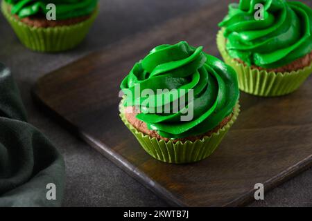 Cupcake al cioccolato con panna montata verde e spolverini al cioccolato su sfondo marrone per St. Giorno di Patrick. Primo piano. Foto Stock