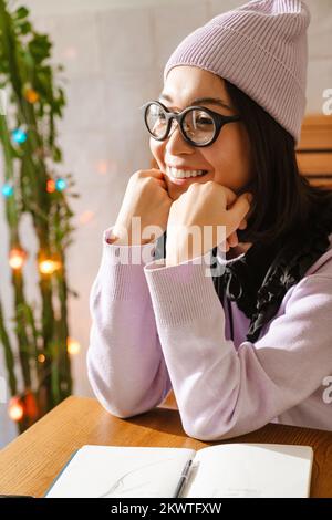 Giovane donna asiatica sorridente mentre si siede al bar Foto Stock