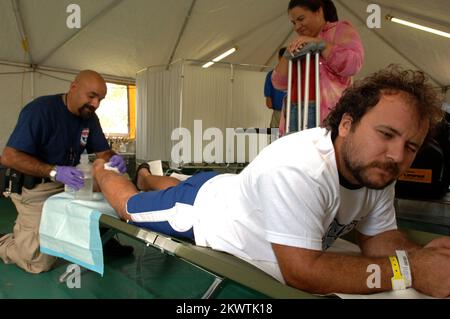 Hurricane Wilma, Plantation, FL, 28 ottobre 2005 George Schiopulescu, A destra, da Lighthouse Point, FL, reagisce al FEMA Disaster Medical Assistance Team paramedico, Carlos Mendoza, a sinistra, mentre pulisce le lacerazioni che Schiopulescu ha ricevuto mentre taglia i detriti causati dall'uragano Wilma. Monica Grigorescu, in piedi, guarda. Il DMAT è stato creato presso il Westside Regional Medical Center per aiutare il flusso di pazienti che visitano il pronto soccorso. Fotografie relative a disastri e programmi, attività e funzionari di gestione delle emergenze Foto Stock