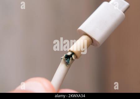 Primo piano tra il cavo del caricabatteria di tipo C bianco rotto e il telefono. Il cavo USB è danneggiato. Foto Stock