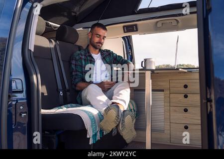 uomo seduto all'interno del suo camper con il telefono Foto Stock