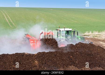 Girando un mucchio di concime sopra fare composto per spargere su terreno agricolo, che aiuta ad aumentare la qualità del suolo. North Yorkshire, Regno Unito. Foto Stock