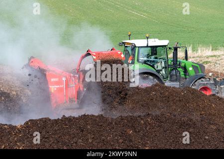 Girando un mucchio di concime sopra fare composto per spargere su terreno agricolo, che aiuta ad aumentare la qualità del suolo. North Yorkshire, Regno Unito. Foto Stock