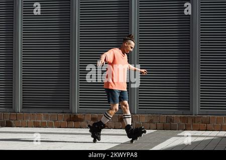Vista laterale del giovane uomo in pantaloncini corti e t-shirt facendo trucco sui pattini a rotelle all'aperto, immagine stock Foto Stock