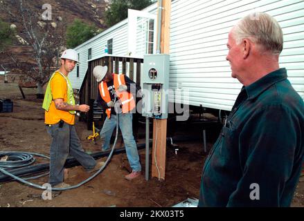 Incendi selvatici, Delzura, CA, 5 dicembre 2007 il candidato FEMA Jon Grice, a destra, orologi come elettricisti Adam Murschel, a sinistra, e Franklin WOOOD, entrambi di o'Donnell Electric, installare il cablaggio per la casa mobile Grice e sua moglie vivranno temporaneamente in mentre iniziano la ricostruzione. La coppia ha perso la propria casa durante i fuochi d'incendio di ottobre. Amanda Bicknell/FEMA.. Fotografie relative a disastri e programmi, attività e funzionari di gestione delle emergenze Foto Stock