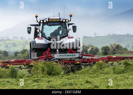 Il fornitore guida un trattore Valtra e sparge erba in un campo insilato con un tagliatappe Pottinger. Dumfries, Regno Unito. Foto Stock