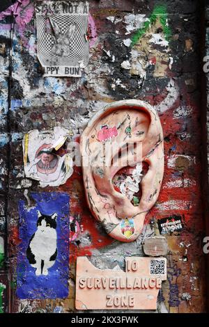 poster, pittura, graffiti e un orecchio di plastica su un muro a Shoreditch, Londra Foto Stock